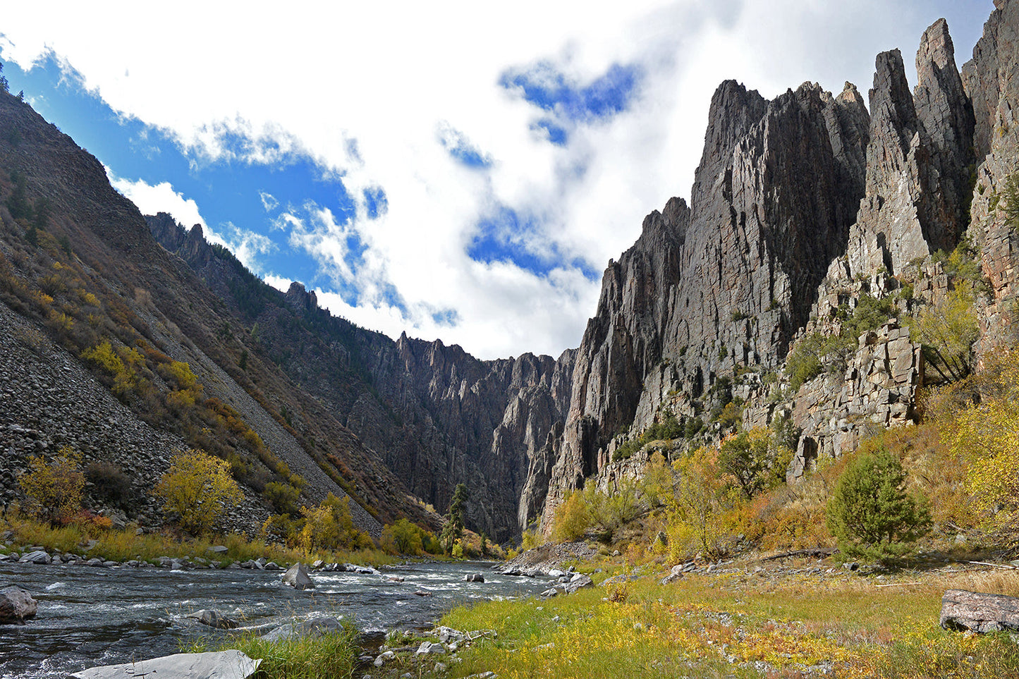 A photo of a river through a canyon with a cloudy and blue sky